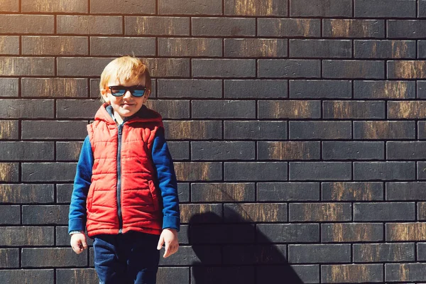 Mode kid buitenshuis, dragen in de rode vest en zonnebril. — Stockfoto