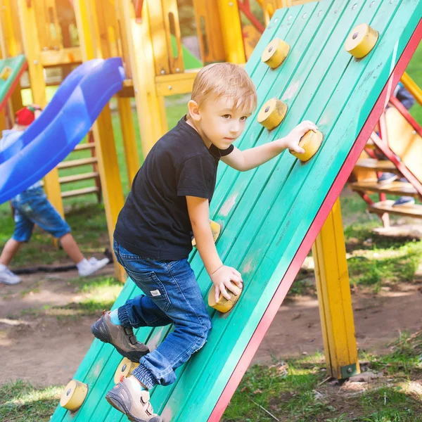 Netter kleiner Junge hat Spaß und klettert auf Spielplatz. — Stockfoto