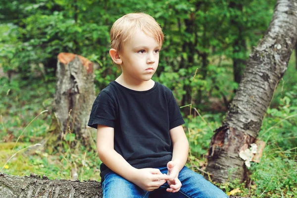 Fatigué liitle garçon assis sur une bûche pour se reposer dans une forêt . — Photo