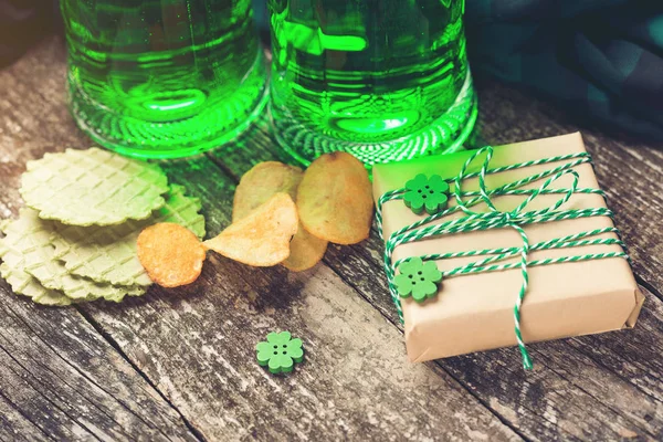 St. Patrick 's Day Hintergrund mit zwei Bechern mit grünem Bier, Snack und Geschenk-Box für die Feier. — Stockfoto