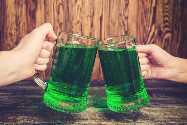 Amigos, segurando duas canecas de cerveja verde contra a parede de madeira . — Fotografia de Stock