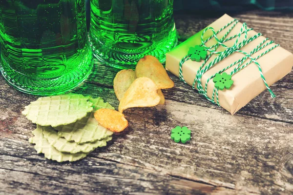 St. Patrick's Day background with two mugs of green beer, snack and gift box for celebration. — Stock Photo, Image