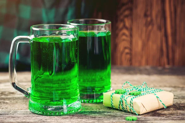 Fundo do Dia de São Patrício com duas canecas de cerveja verde, lanche e caixa de presente para celebração . — Fotografia de Stock