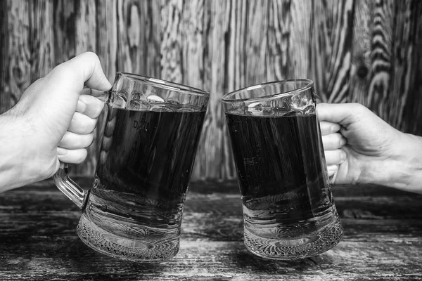 Duas canecas de cerveja verde nas mãos contra uma parede de madeira. Foto em preto e branco . — Fotografia de Stock