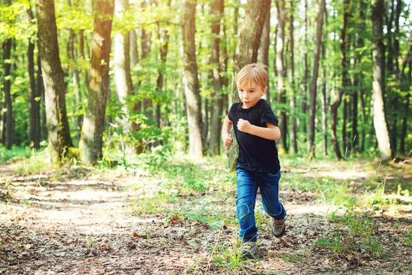 Feliz chico rubio corriendo en un día soleado en el bosque . — Foto de Stock