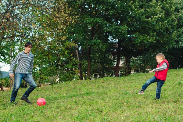 Jovem pai com seu filhinho jogando futebol no gramado verde . — Fotografia de Stock