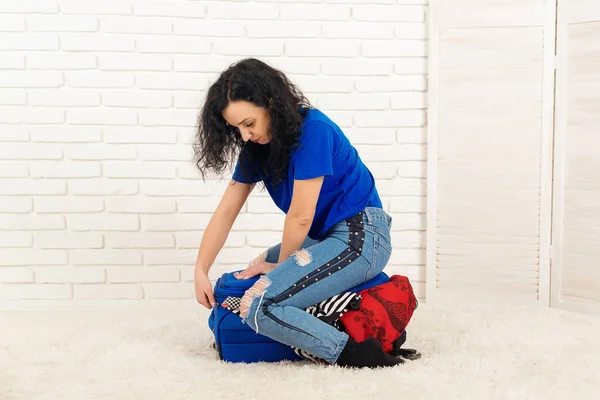 Молода жінка намагається замкнути важку валізу на підлозі . — стокове фото