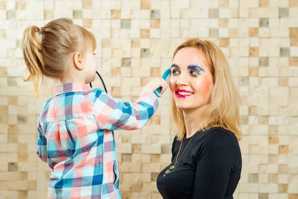 Милая маленькая девочка делает смешной макияж для своей матери . — стоковое фото