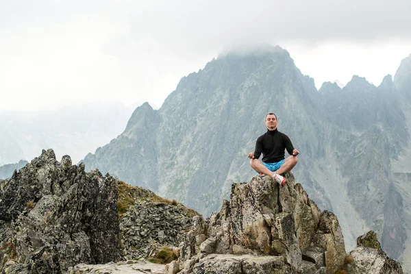 The young man sits on top of the mountain in Lotus pose. — Stock Photo, Image