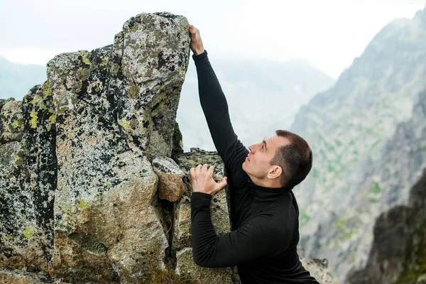 Young man climbs the rock against mountain background. — Stock Photo, Image