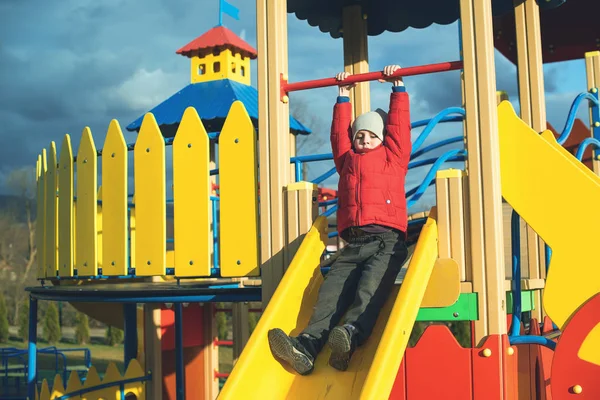 Fröhliche kleine Junge haben Spaß und Rutschen auf bunten modernen Spielplatz im Park. — Stockfoto