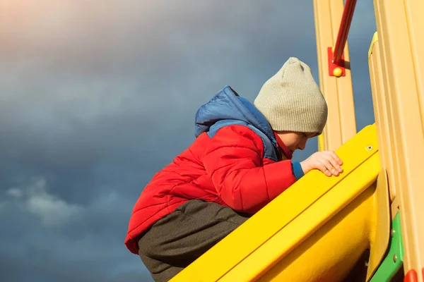 Netter Junge hat Spaß auf Spielplatz im Freien bei kaltem Wetter. — Stockfoto