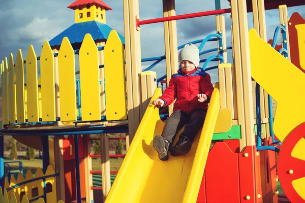 Счастливый мальчик развлекается и катается на разноцветной современной детской площадке в парке . — стоковое фото