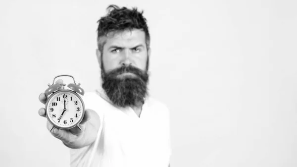 Γενειοφόρος άντρας που κρατάει ξυπνητήρι στον λευκό τοίχο. Συγκεντρώσου στο ρολόι. Αλλάξτε εποχή. Έλεγχος χρόνου — Φωτογραφία Αρχείου