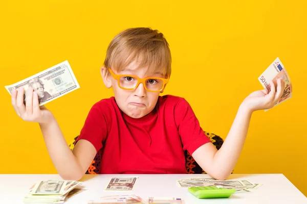 Pequeño niño sosteniendo el dinero y pensando en la creación de nuevos negocios. Pequeño profesor en anteojos con dinero en efectivo sobre fondo amarillo — Foto de Stock