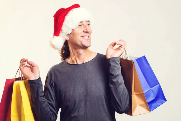 Bonito cara é Papai Noel chapéu auxiliar segurando sacos de compras. Feliz Ano Novo. Presentes de Natal. Tempo de compras de Natal . — Fotografia de Stock