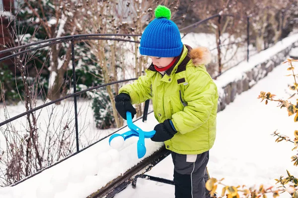 Little boy playing with snowball maker outdoors. Winter fun games at snowy day. Happy winter holidays.