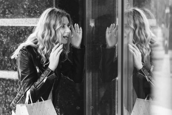 Black Friday. Shocked girl looks through the shop window. Shopping time and great seasonal sales. — Stock Photo, Image