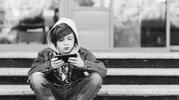 วัยรุ่นที่มีสมาร์ทโฟนนั่งอยู่บนบันไดข้างนอก แนวคิดการเสพติดอินเทอร์เน็ต เด็กชายเล่นเกมมือถือทางโทรศัพท์ . — ภาพถ่ายสต็อก