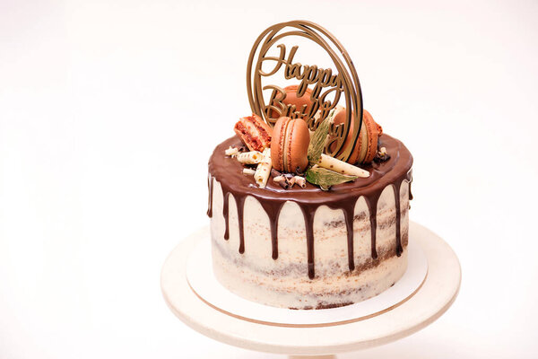 Birthday cake decorated with golden macaroons and chocolate pieces. Elegant naked cake topped by chocolate. 