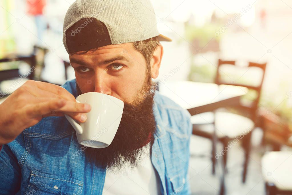 Funny hipster guy drinks coffee. Stylish bearded man at cafeteria outdoors. People, lifestyle and travel concept