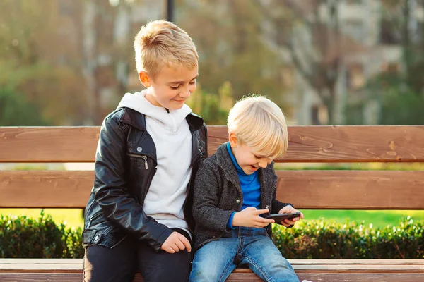 Édes kisfiú videojátékozik okostelefonon. Boldog gyermekek játék online játékok szabadban. — Stock Fotó