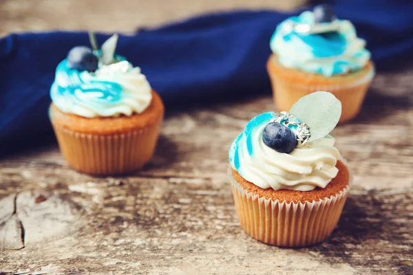 Cupcakes decorados con queso crema azul y bayas frescas. Sabrosos cupcakes con arándanos sobre fondo de madera . — Foto de Stock