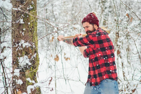 Uomo hipster barbuto che taglia legna nella foresta invernale. boscaiolo nel bosco invernale innevato . — Foto Stock
