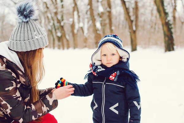 Mother puts on gloves to son in winter park. Woman and her child on a winter walk. — Stock Photo, Image