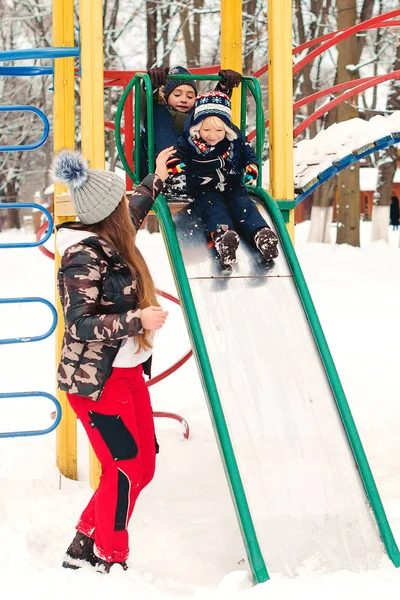 Kinderen hebben plezier op de winterspeelplaats. Wintervakantie. Moeder helpt haar zoontje naar beneden op een glijbaan — Stockfoto