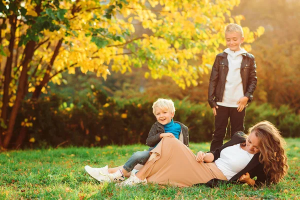 Jovem mãe amorosa com seus dois filhos passando tempo livre ao ar livre. Família, outono moda e estilo de vida — Fotografia de Stock