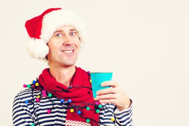 Noel Baba şapkalı gülümseyen adam elinde bir fincan kağıt kahve tutuyor. Noel tatili. Noel satışları ve indirimler