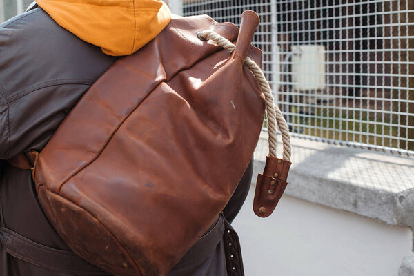 Человек путешествует с кожаным рюкзаком, закрыть. Городской стиль, уличная мода. Модельер с багажом, вид сзади
