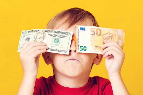 Joyful kid covering eyes with dollar and euro bill over yellow. Happy little boy enjoying his income — Stock Photo, Image