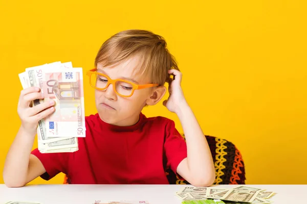 Smart boy counting money at table over yellow background. Future savings — Stock Photo, Image