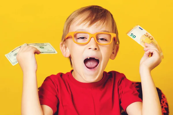 Muchacho emocionado sosteniendo dinero sobre fondo amarillo. Niño inteligente en gafas con efectivo — Foto de Stock