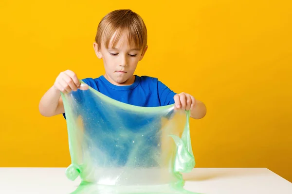 Lapsi leikkii limalla. Onnellinen poika tekee limaa pöydässä. Kotitekoinen suosittu lelu lima. Luovat lapset — kuvapankkivalokuva