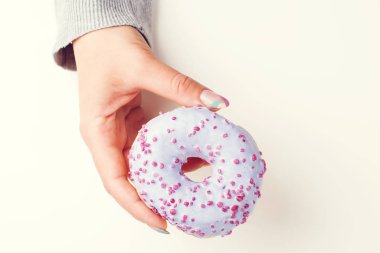Elle tutulur lezzetli donut, üst manzara. Renkli tatlı çörekler serpiştirilmiş. Manikür. Renkli pastel tırnaklı el.