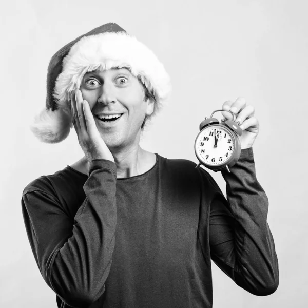 Noel Baba şapkalı yakışıklı adam şok oldu. Çalar saati olan adam. Saat neredeyse on iki. Noel zamanı, satışlar ve indirimler. — Stok fotoğraf