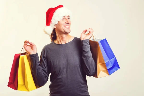 Renkli alışveriş torbalarıyla Noel Baba şapkalı heyecanlı adam. Mutlu noeller. Noel alışverişi zamanı. Mevsimlik satışlar, indirimler ve teklifler — Stok fotoğraf