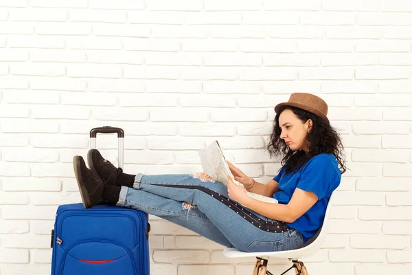 Молодая брюнетка-путешественница в шляпе с голубым чемоданом. Девушка думает о новой поездке — стоковое фото