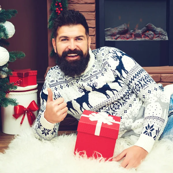 Een man met een baard die met kerst bij de open haard ligt. Cadeaus en groeten voor Kerstmis. Gelukkig Nieuwjaar. Fashion man in kerst trui thuis — Stockfoto