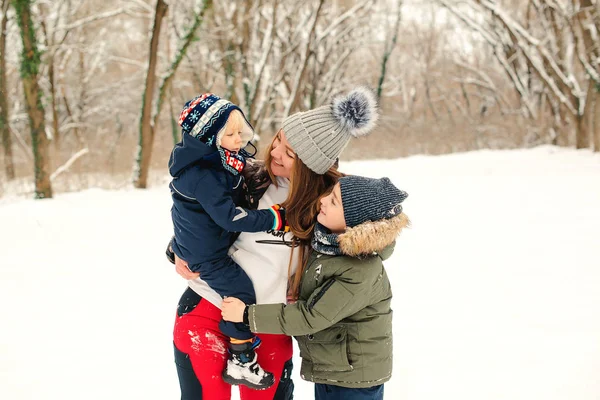 Kedves anya ölelgeti a fiait a Winter Parkban. Boldog gyerekek és anya télen sétálnak. Boldog család élvezi a téli ünnepeket — Stock Fotó