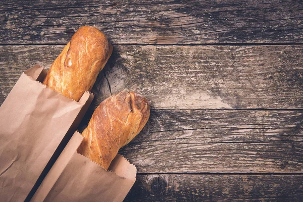 Fresh french baguettes in paper bags on wooden background, copy space. Bread shop.