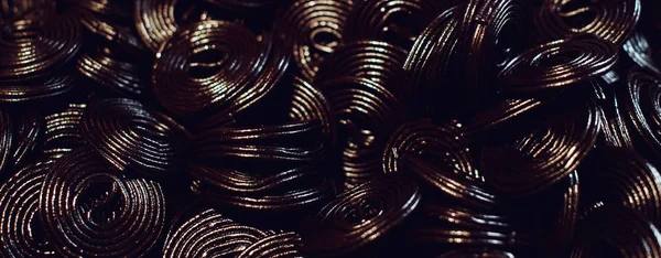 Candy shop. Street market. Dark jelly flavored licorice. Top view. Black candy spiral background.