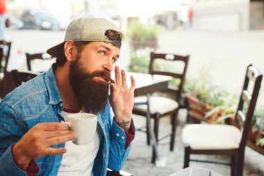 Sakallı hippi bir fincan kahveyle masada oturuyor. Yakışıklı adam terasta kahve içiyor.