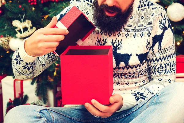 Şok olmuş bir adam Noel 'de hediye kutularını açıyor. Heyecanlı sakallı adam hediyesini ağzı açık tutuyor. Noel hediyeleri zamanı. — Stok fotoğraf