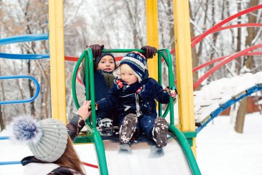 Happy kids having fun on playground at winter. Winter leisure outdoor activities. Mother with two son on a winter walk.