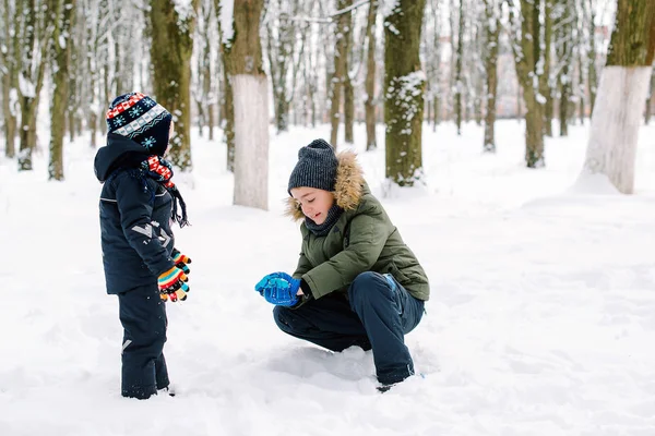 Older brother teaches to make snowballs younger brother. Happy family vacation. Kids playing with snow — Stok fotoğraf