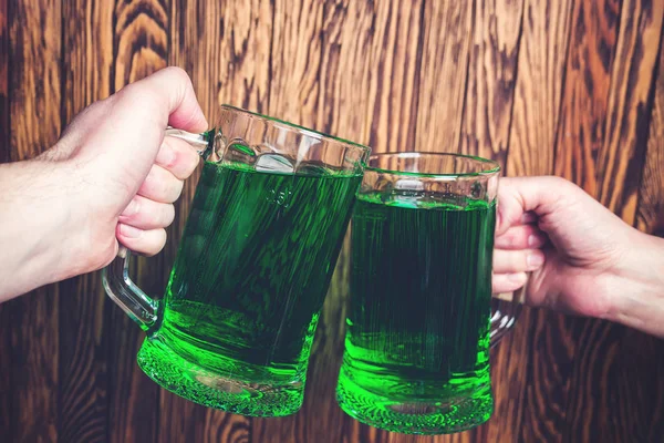 Friends toast with each other. Saint Patrick\'s day party. Group of friends is celebrating. Happy people is drinks a green beer